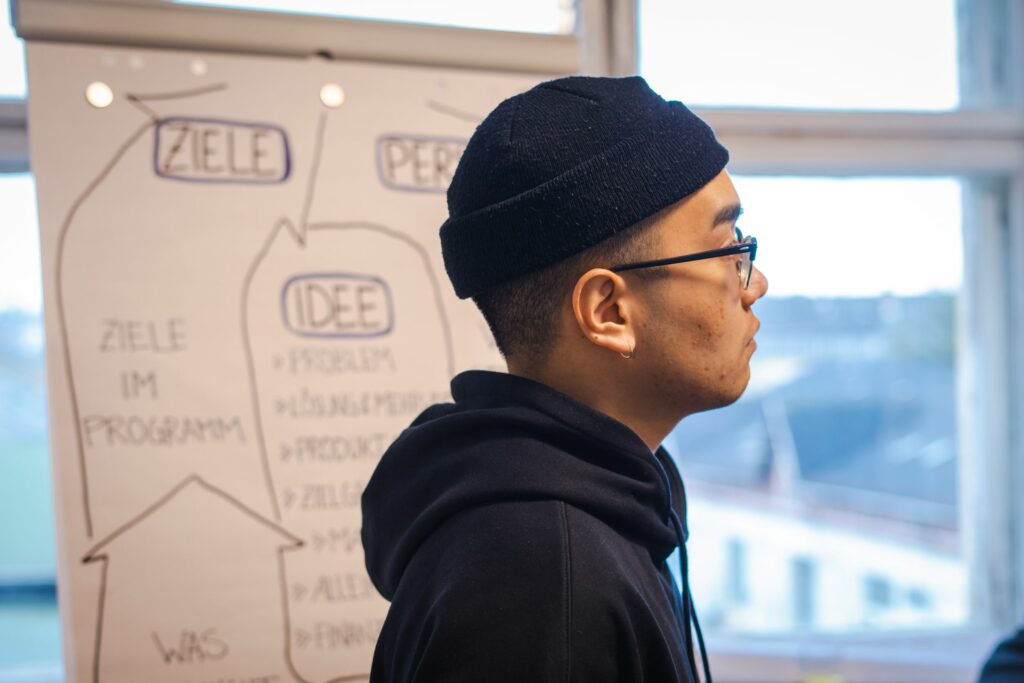 Scholarship holder in the foreground. In the background, a flip chart thematically dealing with goals. 